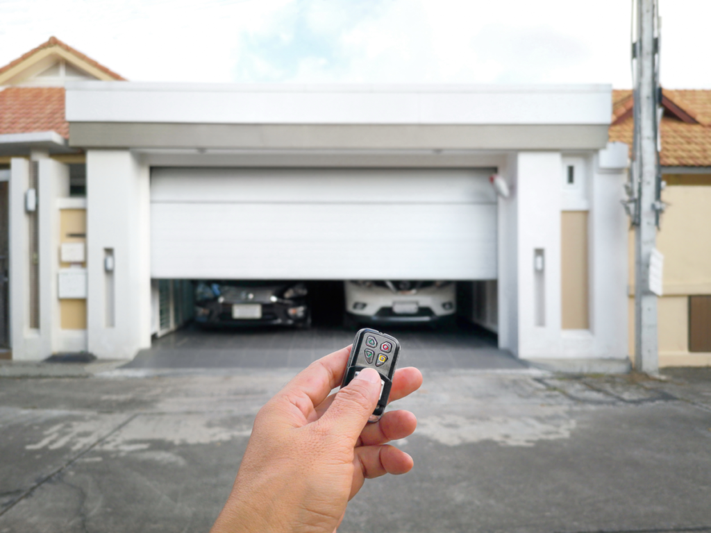 A hand pointing a garage door opener at a garage door.